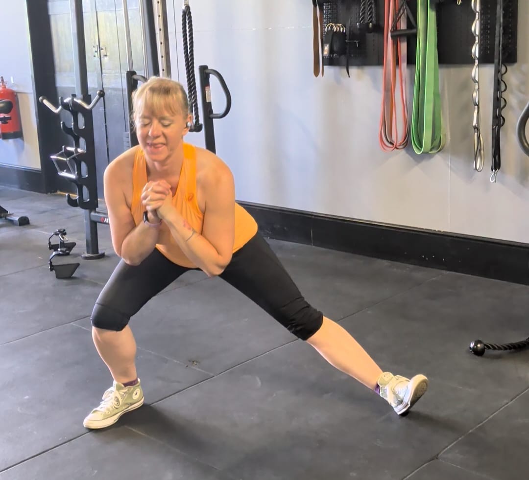 Andrea demonstrating a Cossack squat, weight shifted onto one bent leg with the opposite leg extended straight out to the side.