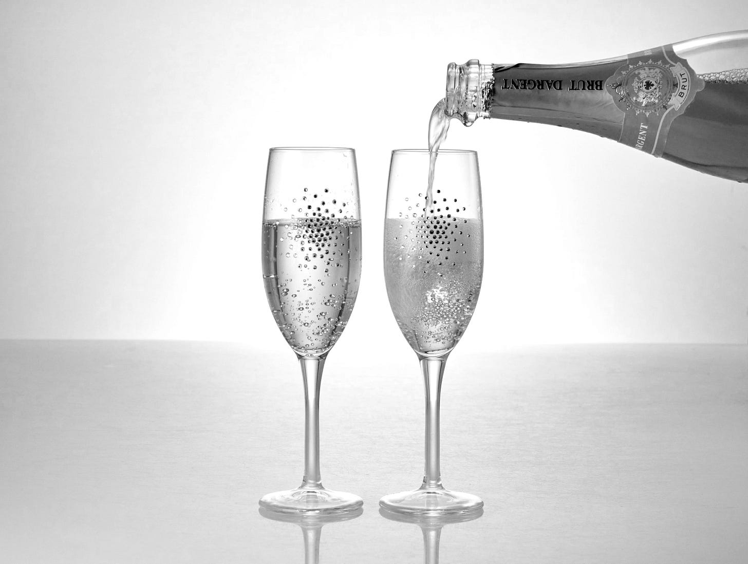 A bottle of champagne being poured into two wine glasses A bottle of champagne being poured into two wine glasses