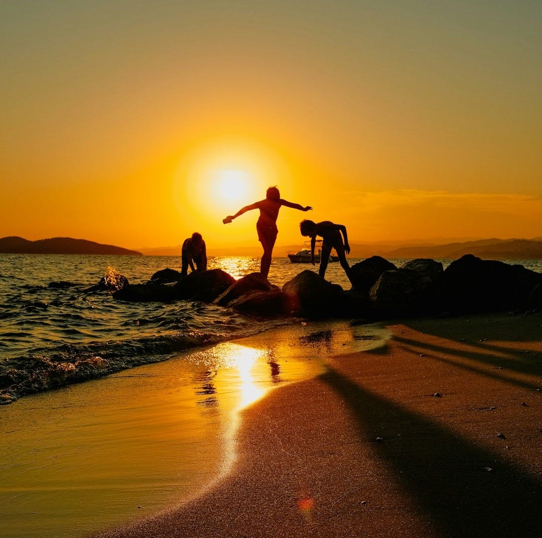 Silhouettes of people on rocks at sunset beach Silhouettes of people on rocks at sunset beach