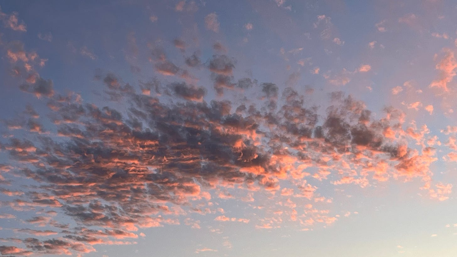 Fragmented cloud coloured salmon pink and grey against a pale blue sky at midsummer sunset