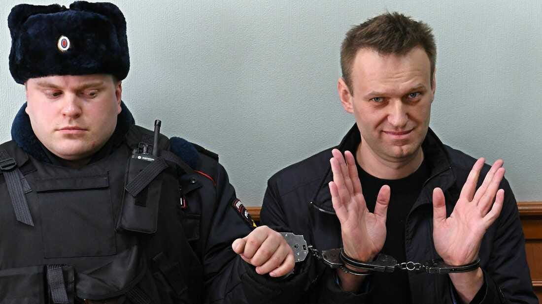 A person in handcuffs with a police officer in the background

Description automatically generated