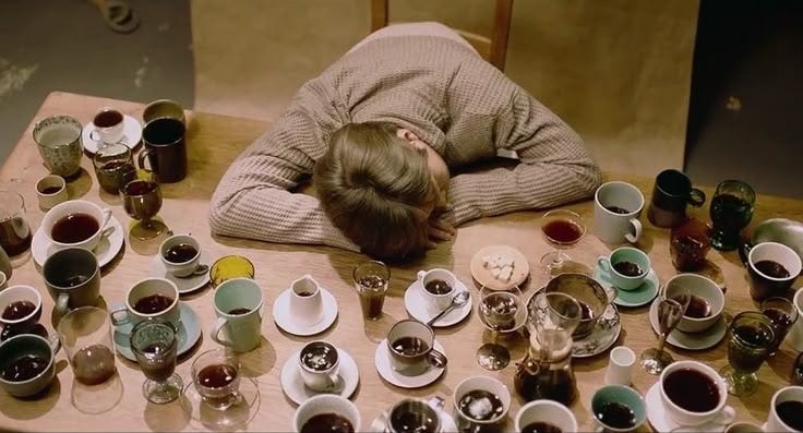 This may contain: a person is sleeping on a table with cups and saucers all over it,