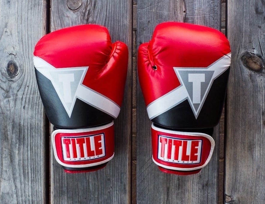 pair of red-and-black Title training gloves on grey wooden plank pair of red-and-black Title training gloves on grey wooden plank