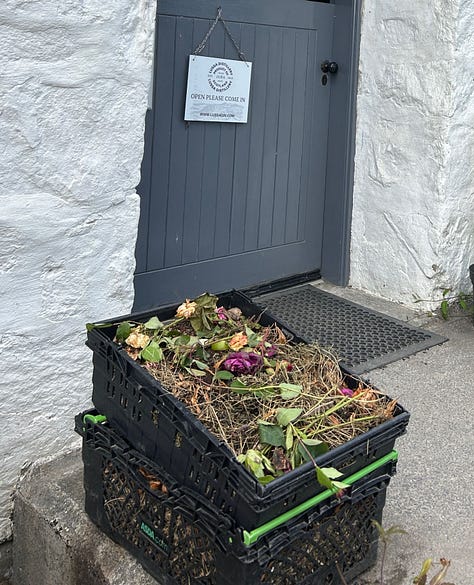 A box of flowers and leaves, a large copper still, shelves of bottles for sale