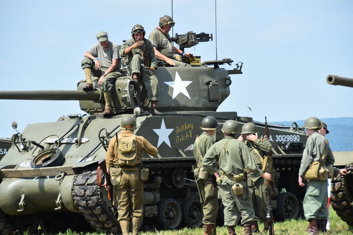 Men dressed in WWII attire stand around a tank that has a big white star on the side.