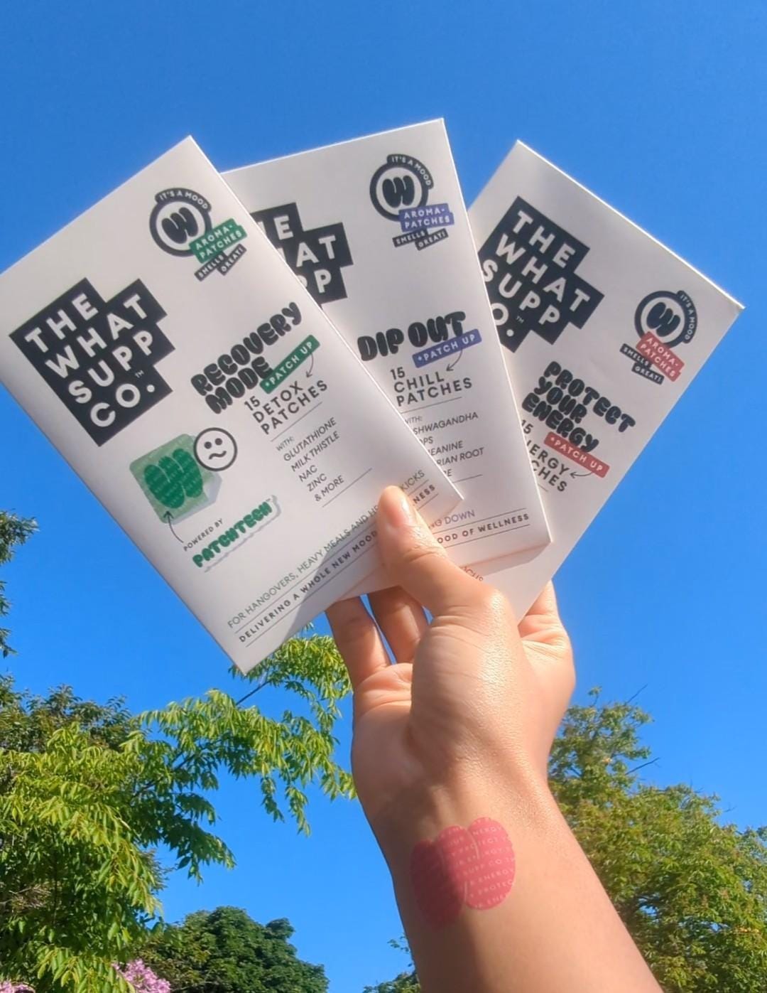 Hand holding packets of patches against a backdrop of a blue sky