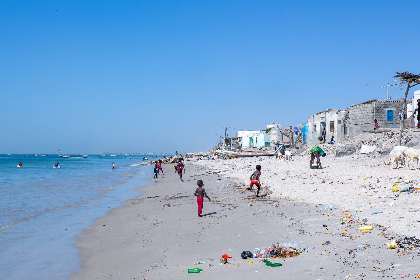 Children play on a beach in Senegal near several homes.