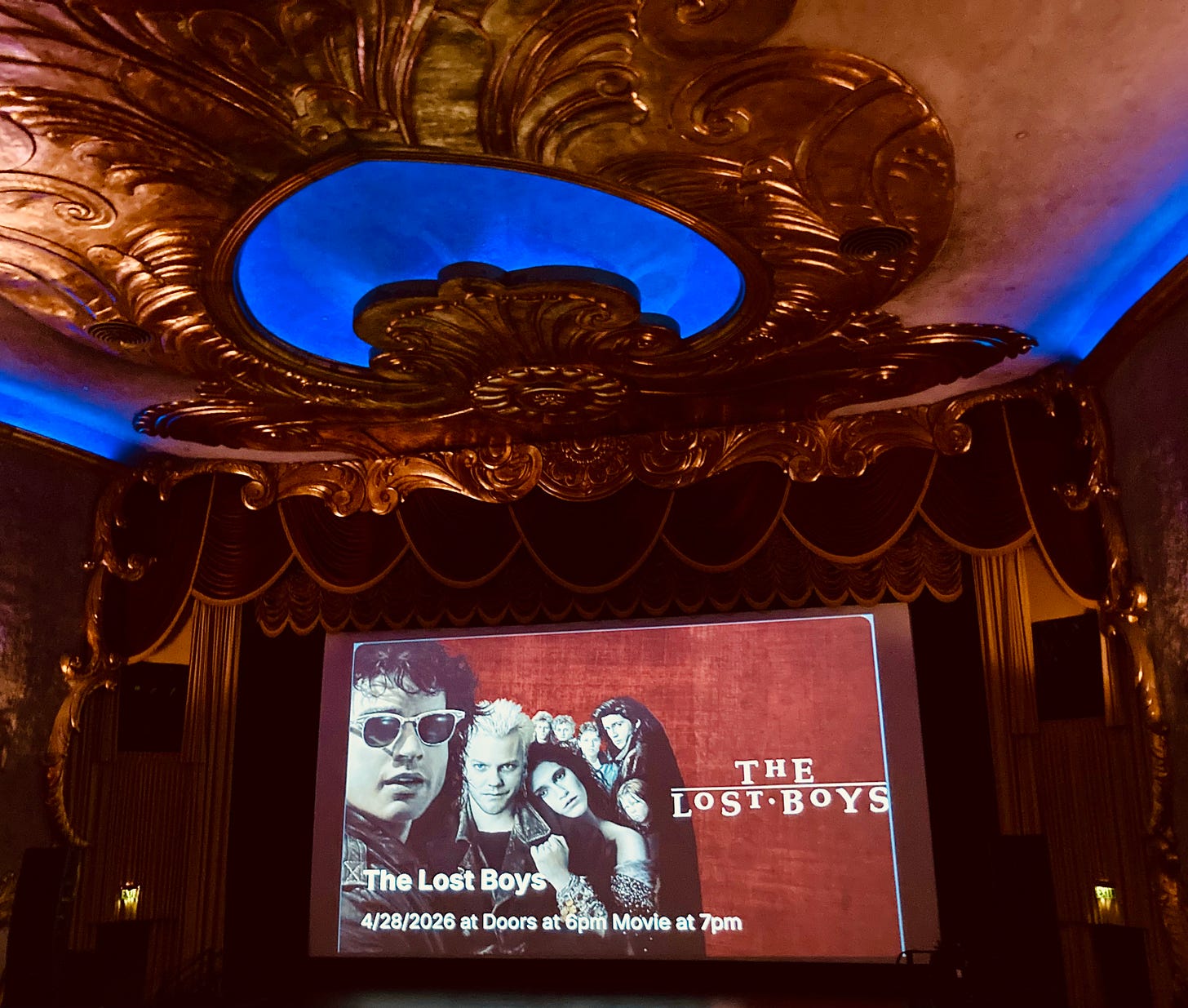 Interior of historic theater with gold embellishments on the ceiling, a curtain around the screen, and a promotional image for the screening of "The Lost Boys" Interior of historic theater with gold embellishments on the ceiling, a curtain around the screen, and a promotional image for the screening of "The Lost Boys"