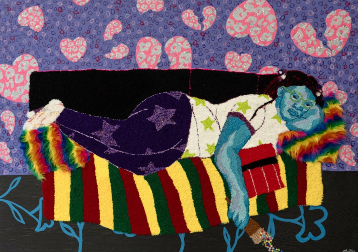 A blue figure lounges on a striped couch with rainbow pillows against a wall filled with pink broken-heart patterns.