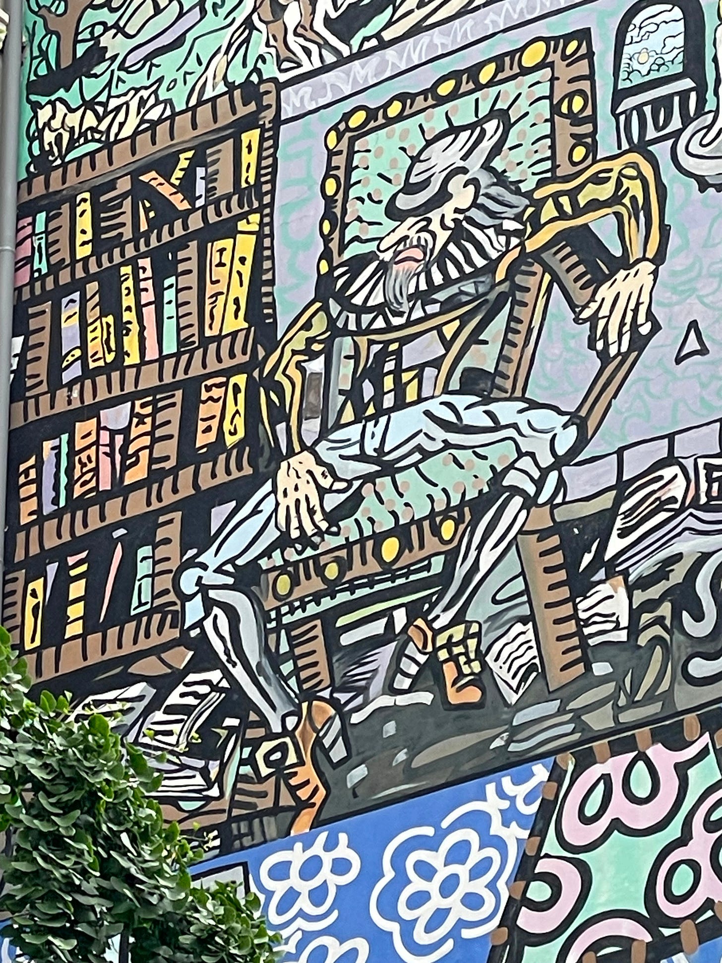 Colourful street art of an abstract kinda dude sitting next to a bookshelf with a frame around his face