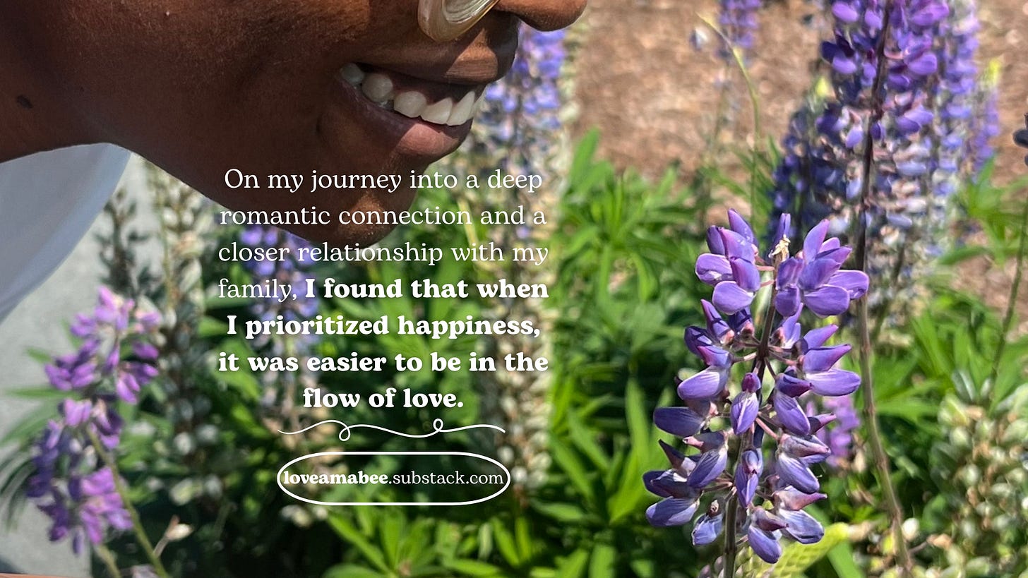 On my journey into a deep romantic connection and a closer relationship with my family, I found that when I prioritized happiness, it was easier to be in the flow of love. Woman admires purple flowers with a smile. 