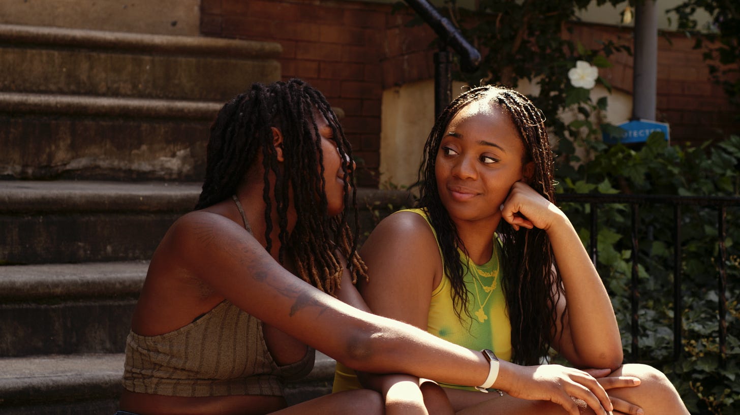 Still image from “Be Back By 3” by Aliyah Dominique Jefferies. The lead characters sit are sitting on steps outdoors looking at one another lovingly. Still image from “Be Back By 3” by Aliyah Dominique Jefferies. The lead characters sit are sitting on steps outdoors looking at one another lovingly.