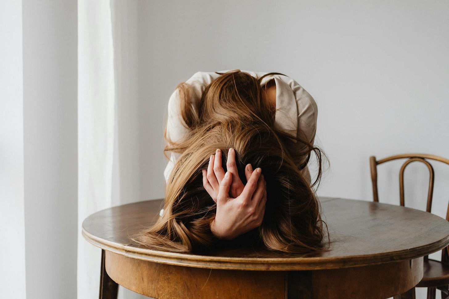 A frustrated woman with her head on the table and her hands holding the top of her head.