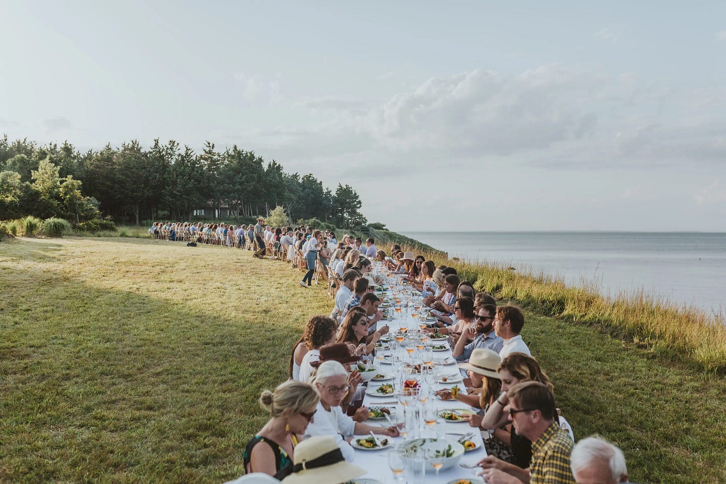 A group of people sitting at a long table with food on it

Description automatically generated