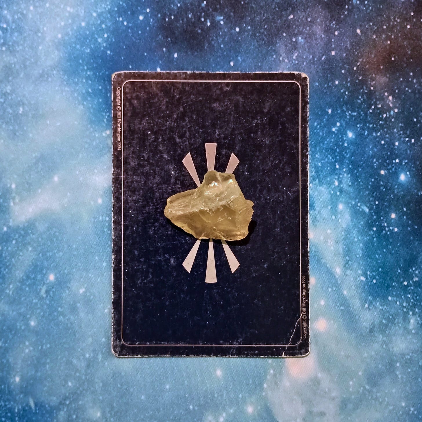 New Moon Magic: Your July 2025 Pick-a-Card Tarot Reading, pile 4 - citrine (yellow) stone and an oracle card, face down, on a starry blue background