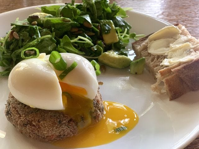 A fried cake with an egg resting on top of it and leaking its yolk over it.