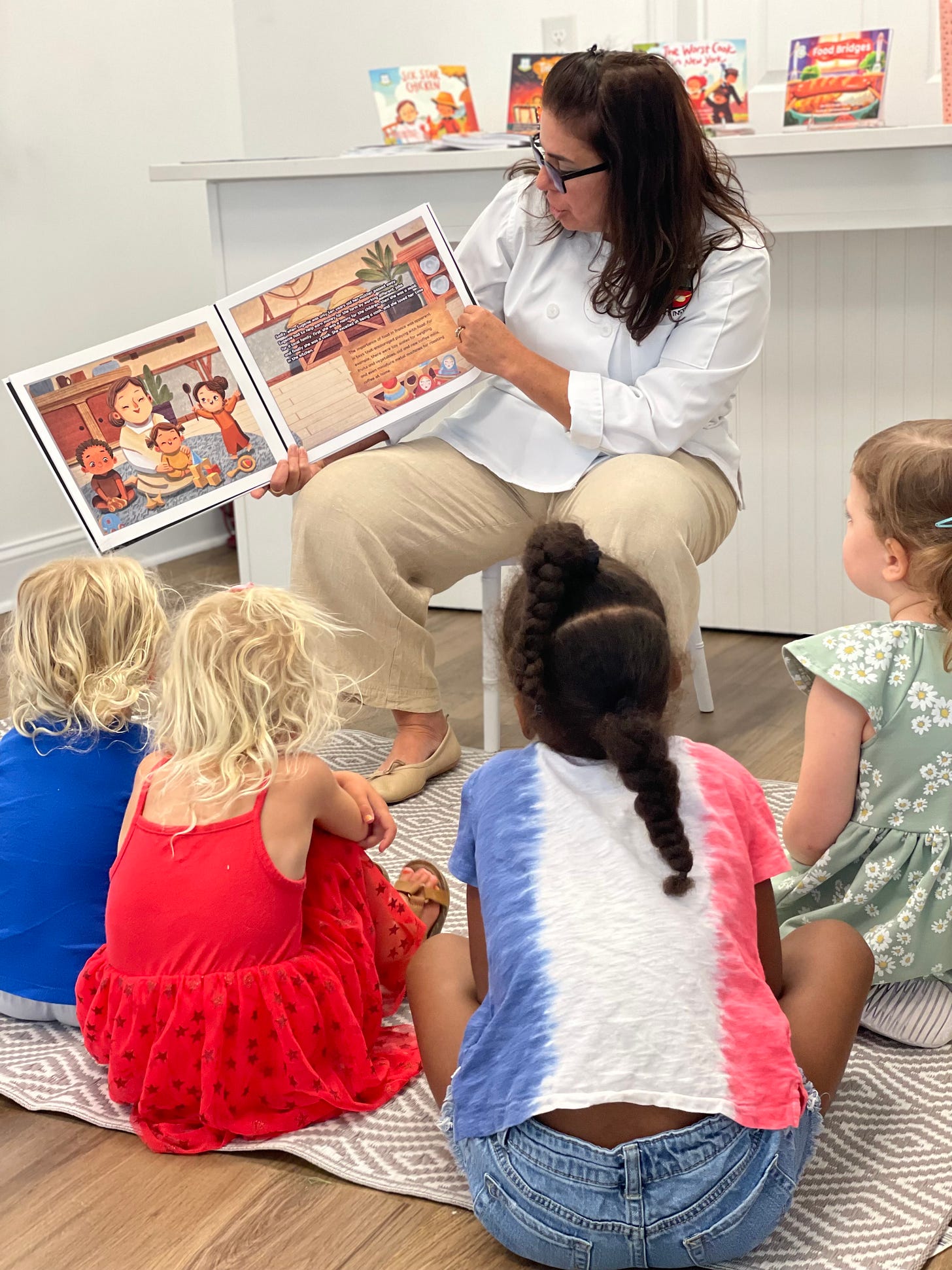 Chef sitting down reading from a book with 4 children watching