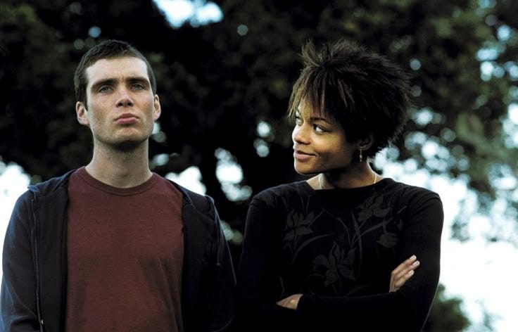 This may contain: a man and woman standing next to each other in front of trees with their arms crossed