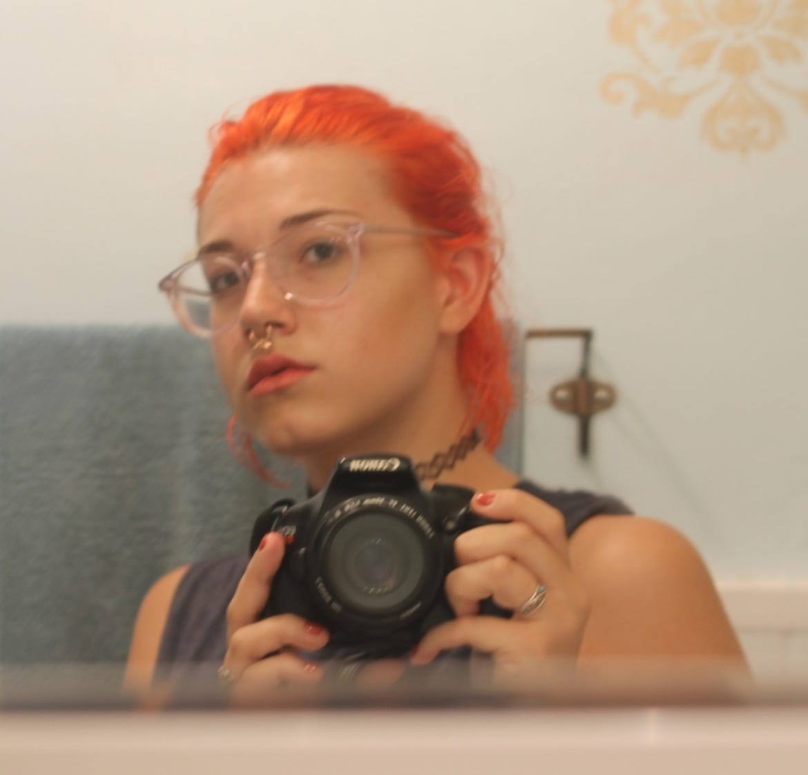 selfie of the author with bright orange shoulder length hair and clear round glasses