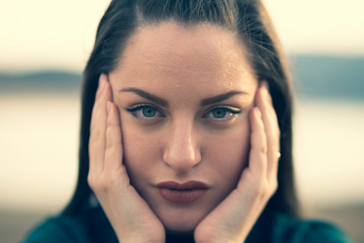 Photo of a woman looking at the camera with her hands on her face. Photo by Nikolay Hristov via Unsplash.