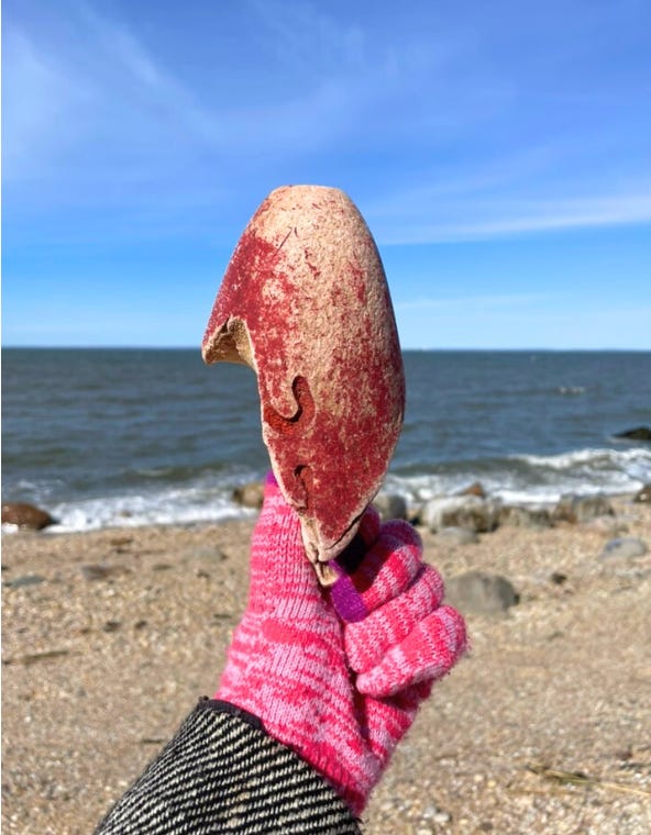 a faded red buoy found at the beach held in a gloved hand