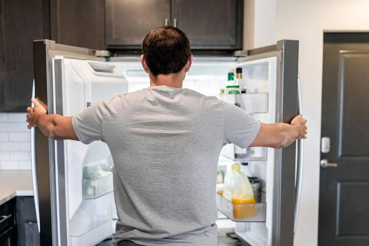 Back view of a man staring into an open fridge. Back view of a man staring into an open fridge.