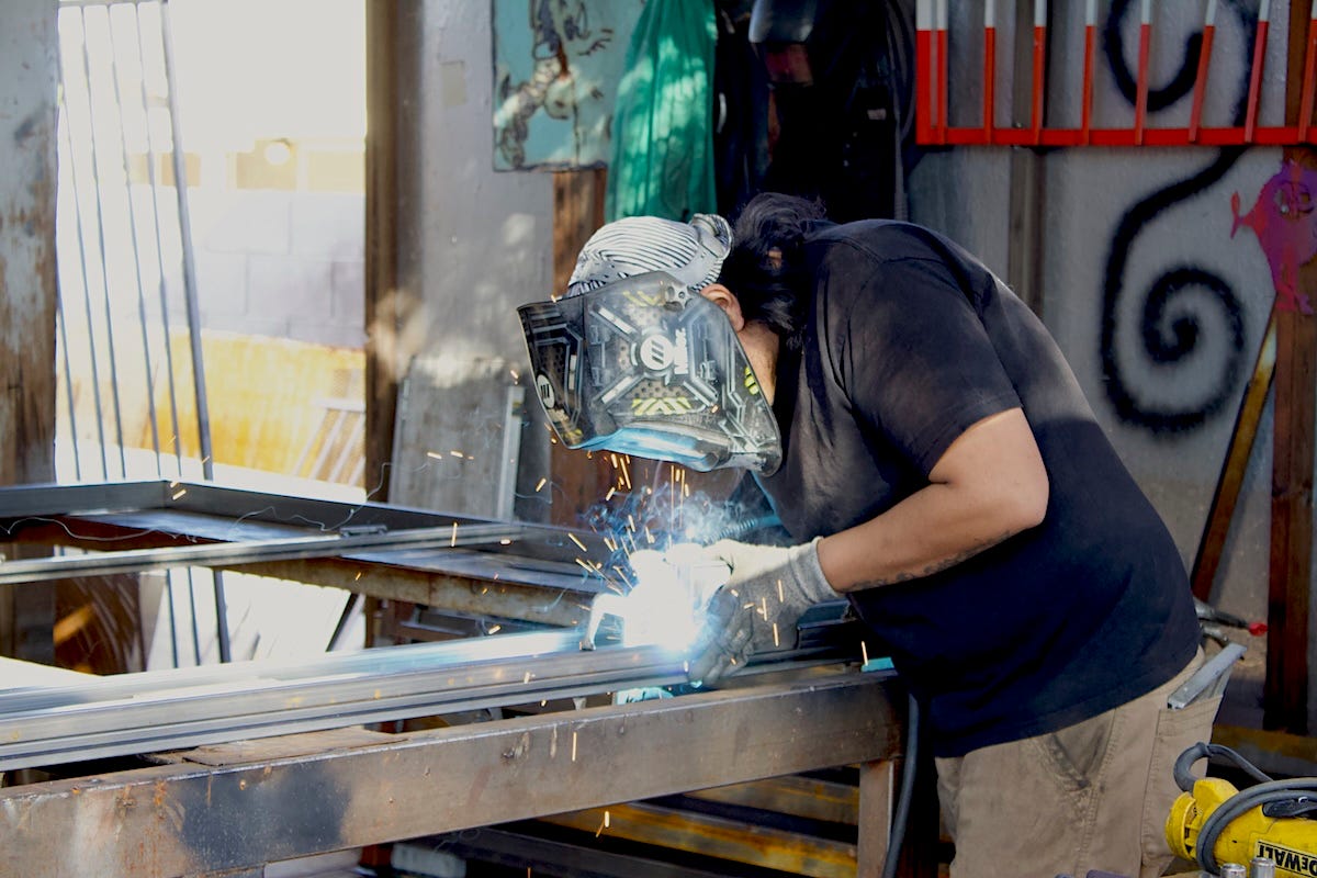 Luis Avila Chavez welding metal in a workshop, sparks flying as he works.