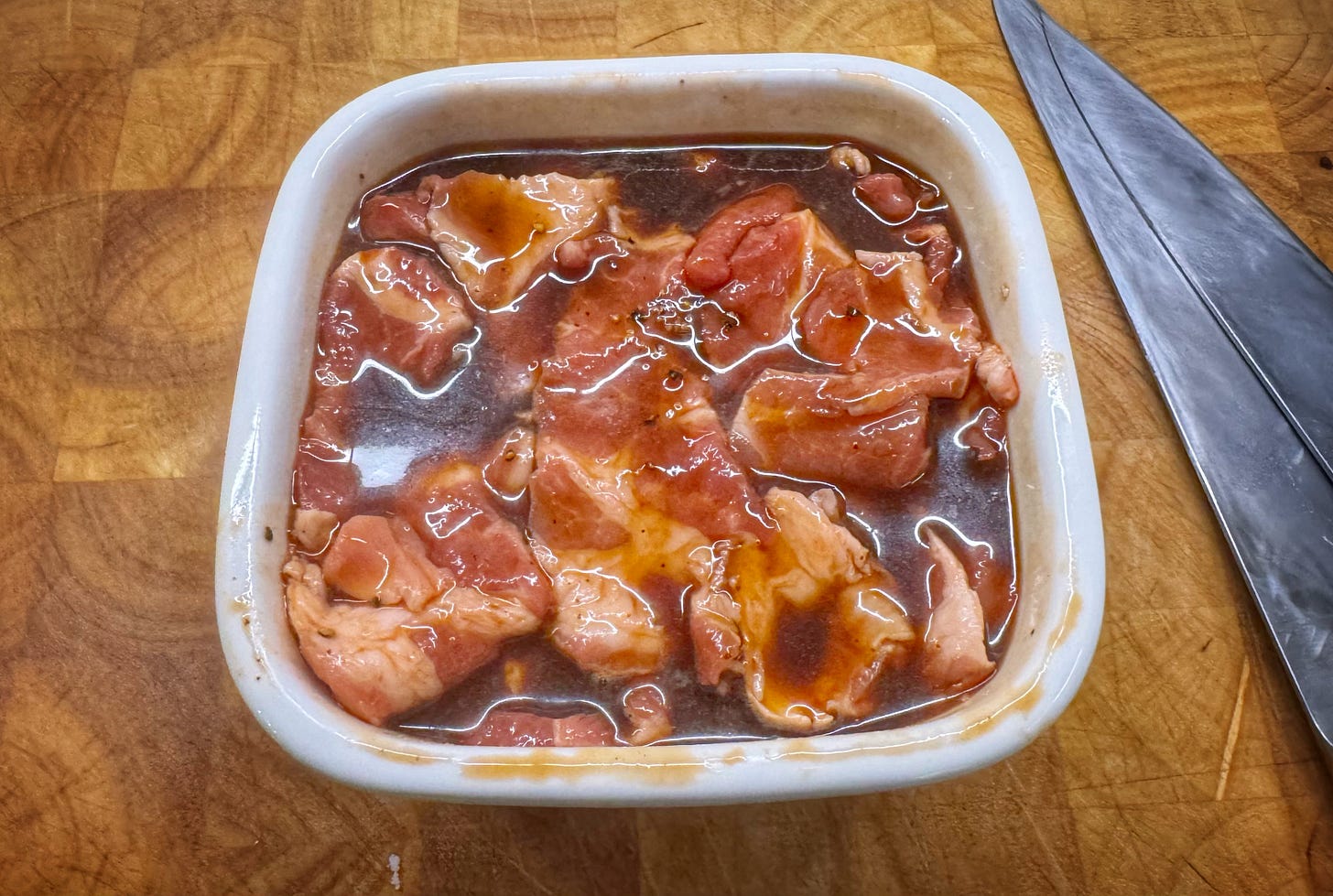 Slices of pork marinating in a ceramic container