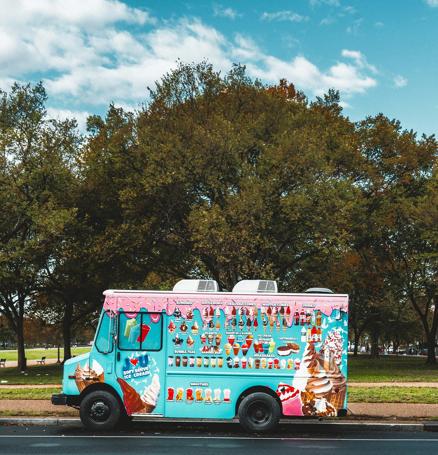 photograph of colorful ice cream truck parked next to trees