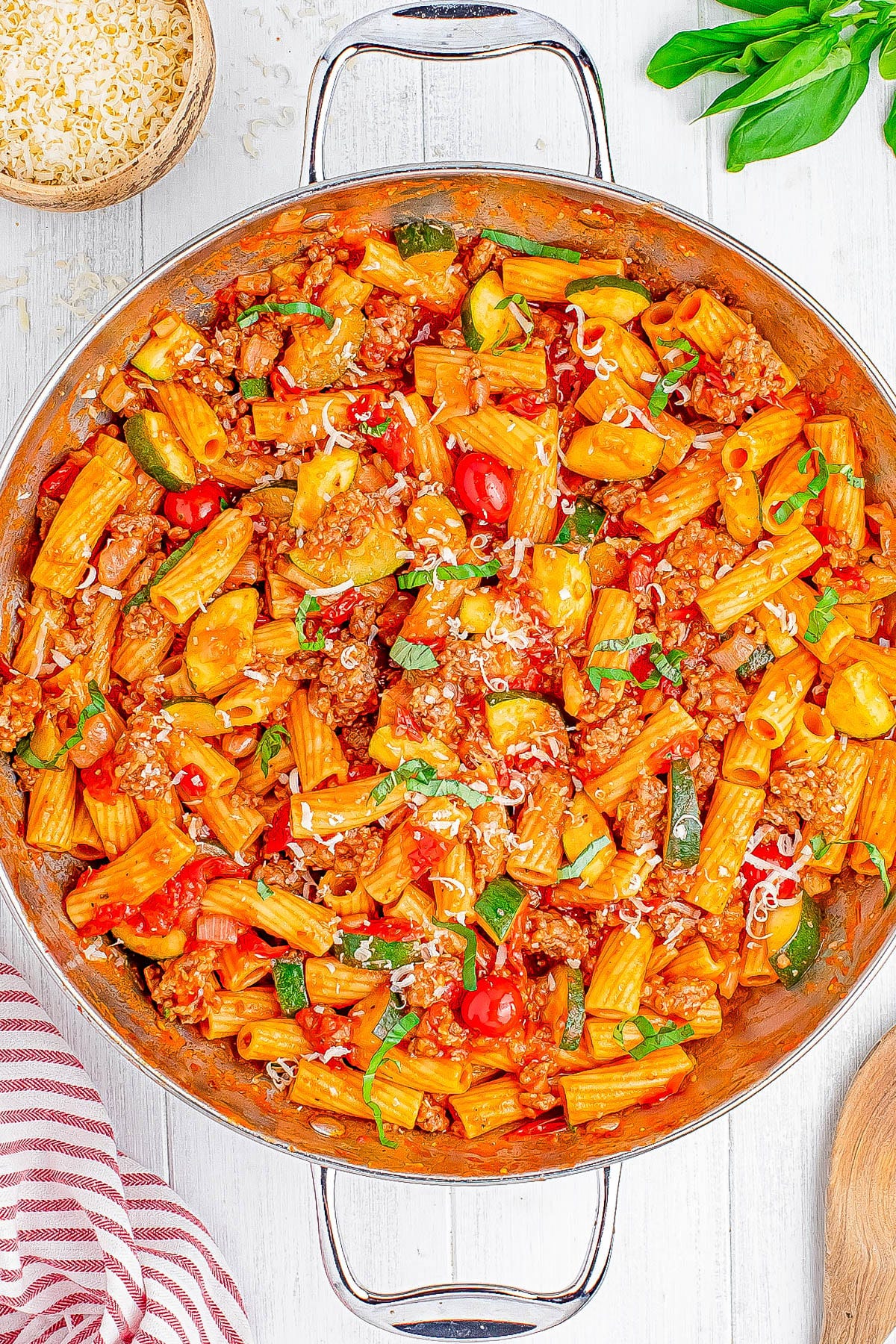 A pan of rigatoni pasta with ground meat, zucchini, cherry tomatoes, and grated cheese, garnished with fresh basil. A pan of rigatoni pasta with ground meat, zucchini, cherry tomatoes, and grated cheese, garnished with fresh basil.