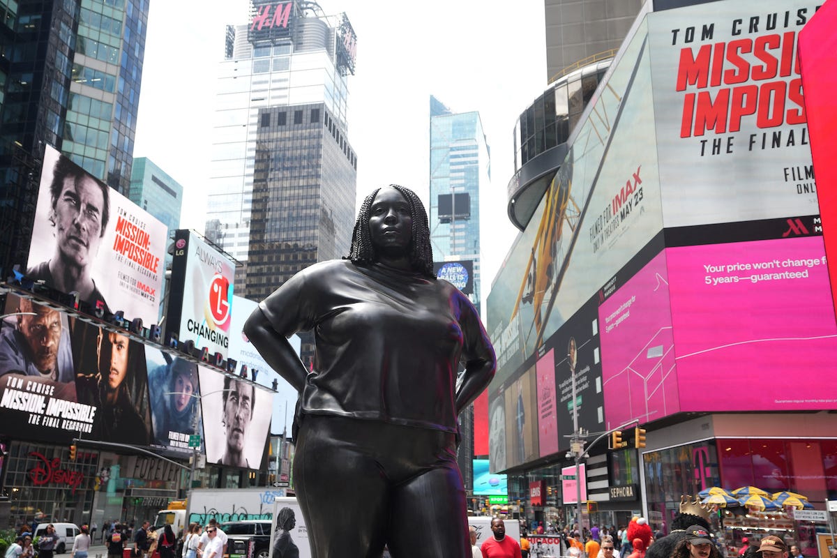 A monumental statue of a Black woman amid ads.