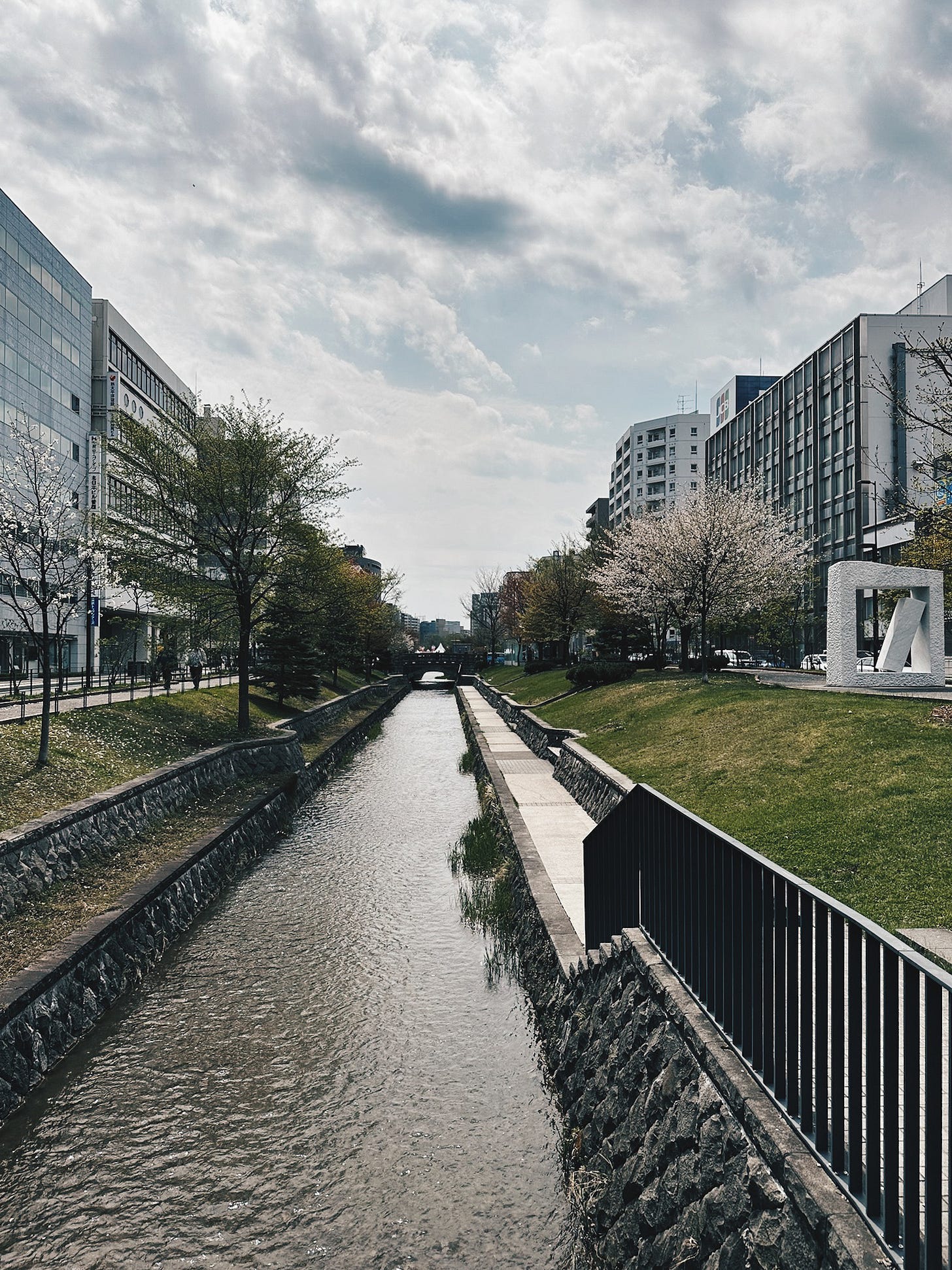 The Sosei River canal running through central Sapporo with cherry blossoms on the bank and dramatic spring clouds overhead. The Sosei River canal running through central Sapporo with cherry blossoms on the bank and dramatic spring clouds overhead.