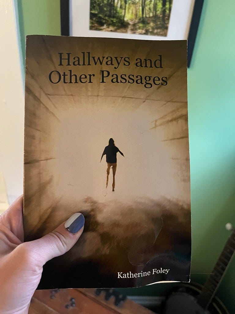 An image of a paperback book called "Hallways and other Passages" with cover art of a person walking into an overexposed light. The book is being held by a person with a patterned manicure in front of a light green wall and a window on the left and a framed photo of a forest above it.