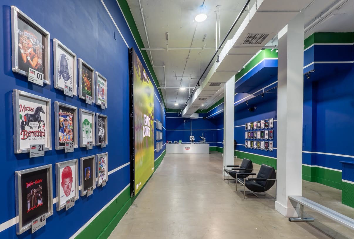 Interior of The Unofficial Shop in New York, with dozens of independently designed tennis T-shirts displayed across blue and green walls. Interior of The Unofficial Shop in New York, with dozens of independently designed tennis T-shirts displayed across blue and green walls.