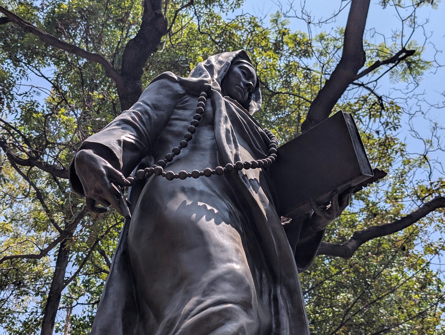 Bronze statue of Sor Juana Inés de la Cruz on a stone pedestal along the Paseo de la Reforma sidewalk in Mexico City.