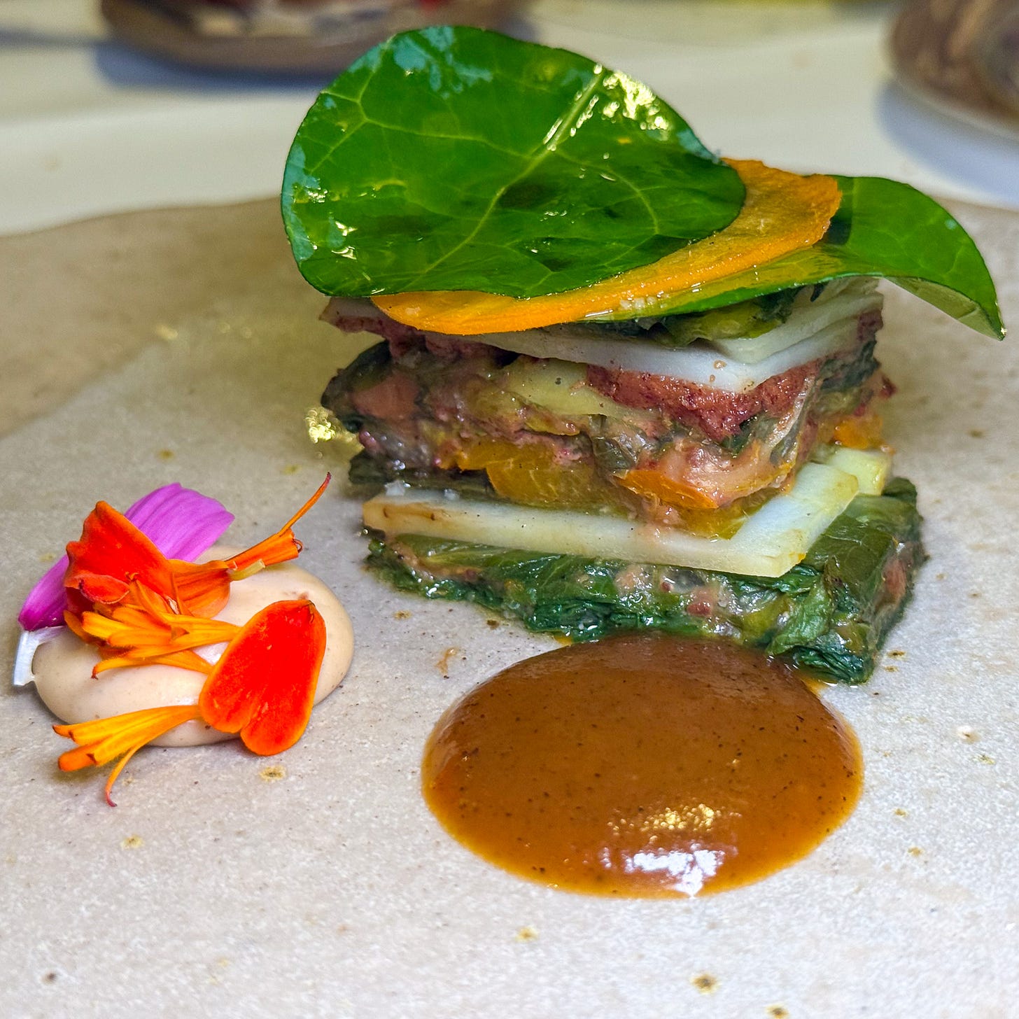 A layered terrine of salad leaves, potato and apricot topped with a lacquered nasturtium leaf, with two sauces, at Datil in Paris. A layered terrine of salad leaves, potato and apricot topped with a lacquered nasturtium leaf, with two sauces, at Datil in Paris.