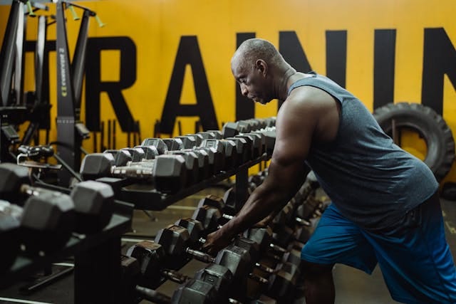 Man in Blue Tank Top Picking From a Set of Dumbbells