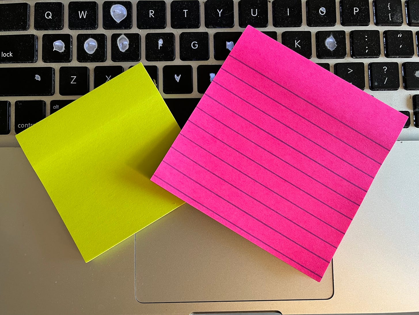Photo of a two neon colored Post-It Notes pads on top of a computer keyboard.