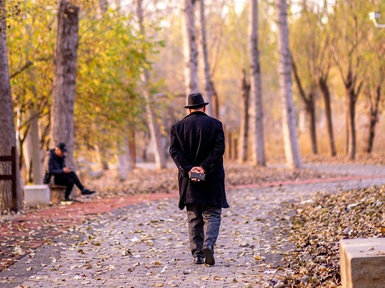 Man in hat walks on autumn path with fallen leaves