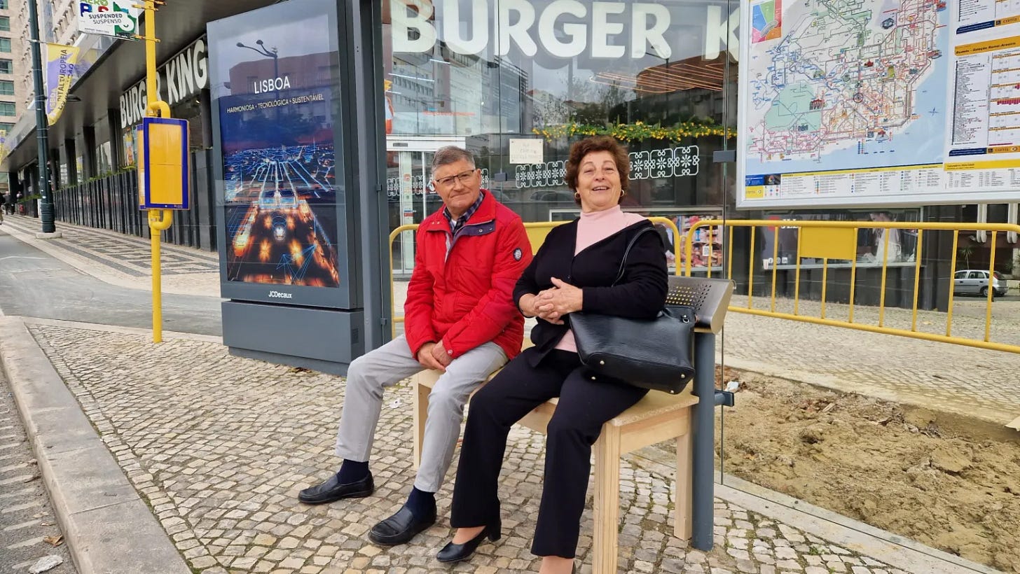 Una coppia di anziani felici è seduta su una panchina di legno alla fermata del bus a Lisbona.