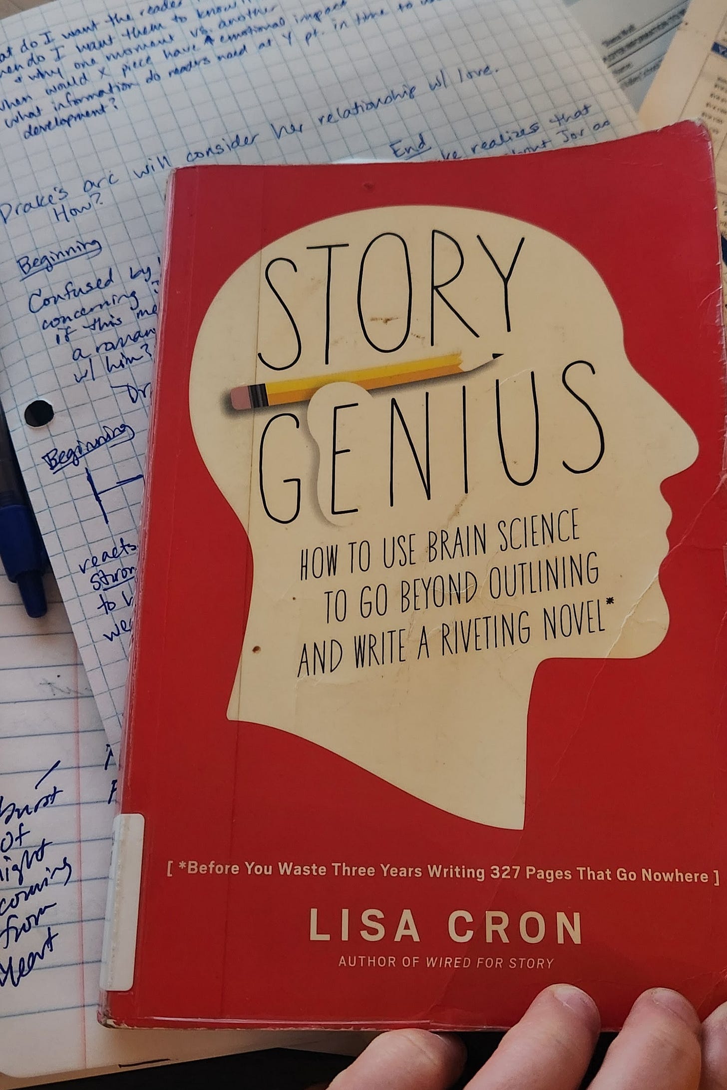 The book, Story Genius by Lisa Cron sits atop a graph paper with writing notes about character arc. The book, Story Genius by Lisa Cron sits atop a graph paper with writing notes about character arc.