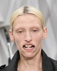 Maison Margiela SS26 models walked the runway wearing metal mouth frames  that stretched their lips into a square. This gesture referenced the four  white seams, Margiela's iconic code, and symbolically silenced facial