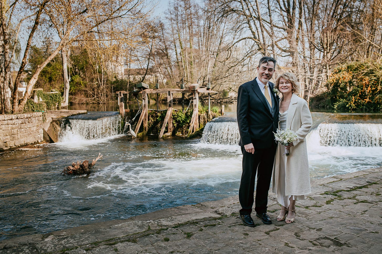 A man and a woman pose for wedding portraits in front of a waterfall in France A man and a woman pose for wedding portraits in front of a waterfall in France