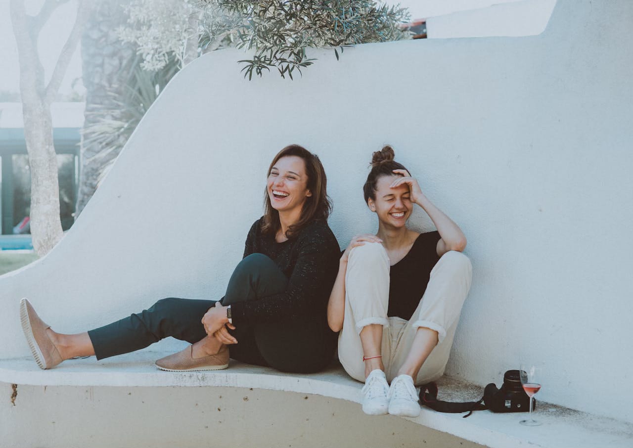 Two women sit on a white bench, laughing. Two women sit on a white bench, laughing.