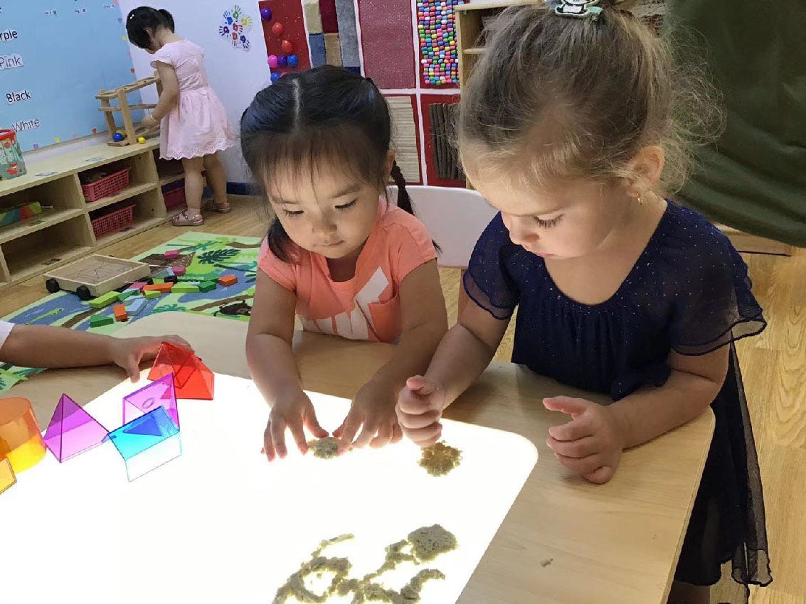 image of two children at a light table, playing with sand and colorful transparent shapes image of two children at a light table, playing with sand and colorful transparent shapes