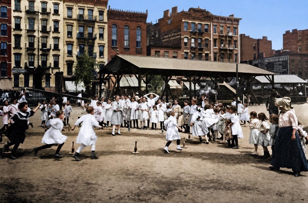 Children play various games in playgrounds with dirt surfaces, surrounded by multi-story brick buildings; some adults supervise in the background.