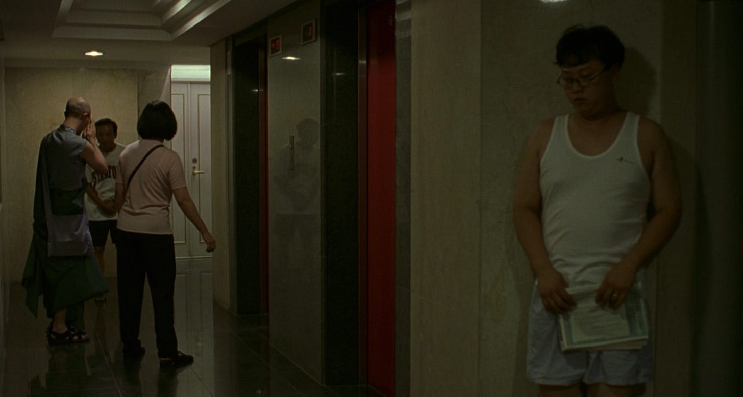 A-Di wears only boxers and a tank-top as he hides around the corner from a religious leader with two other characters in Edward Yang's movie Yi Yi.