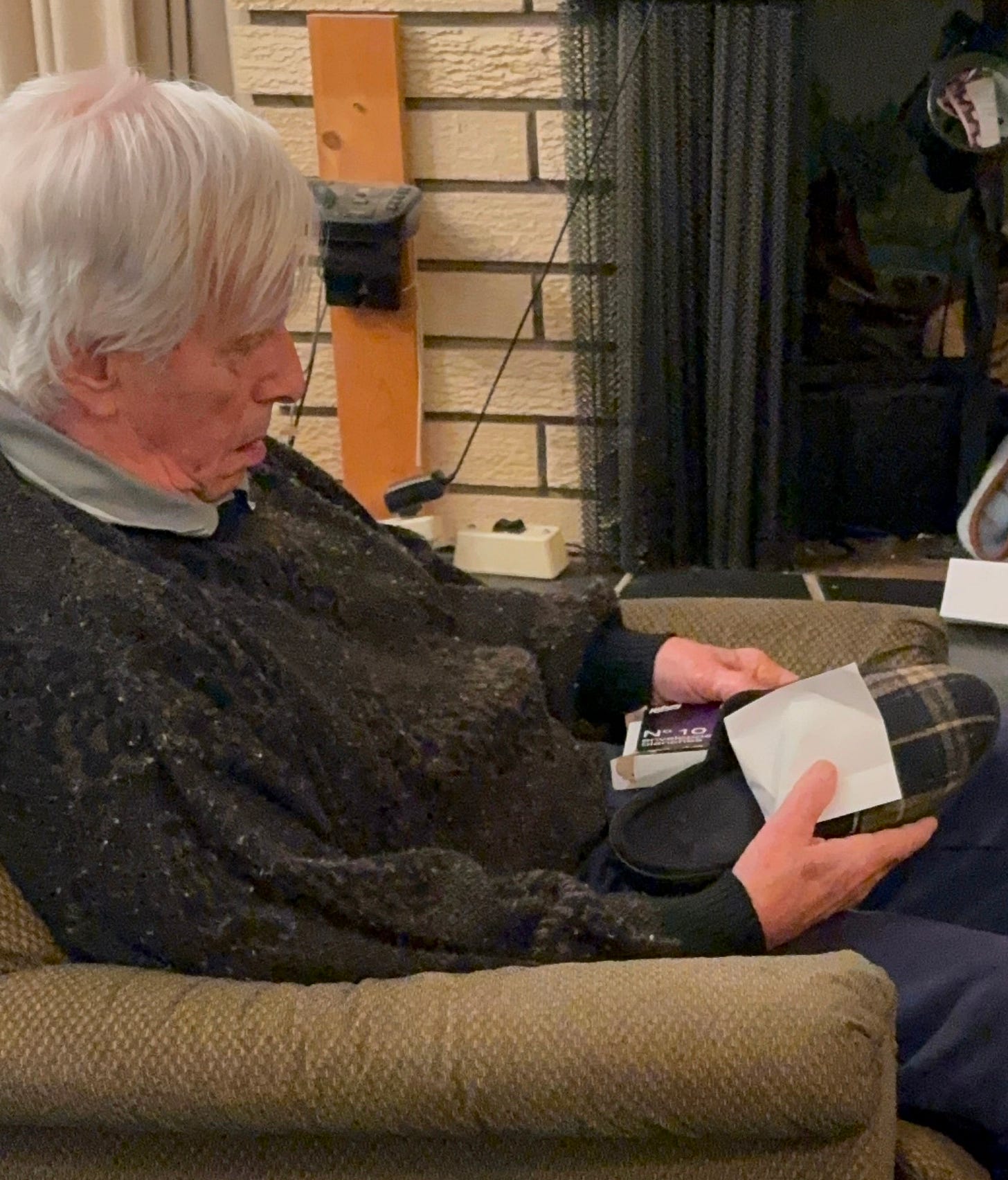 Elderly man sitting in a lounge chair tryingn to stuff envelopes into a slipper