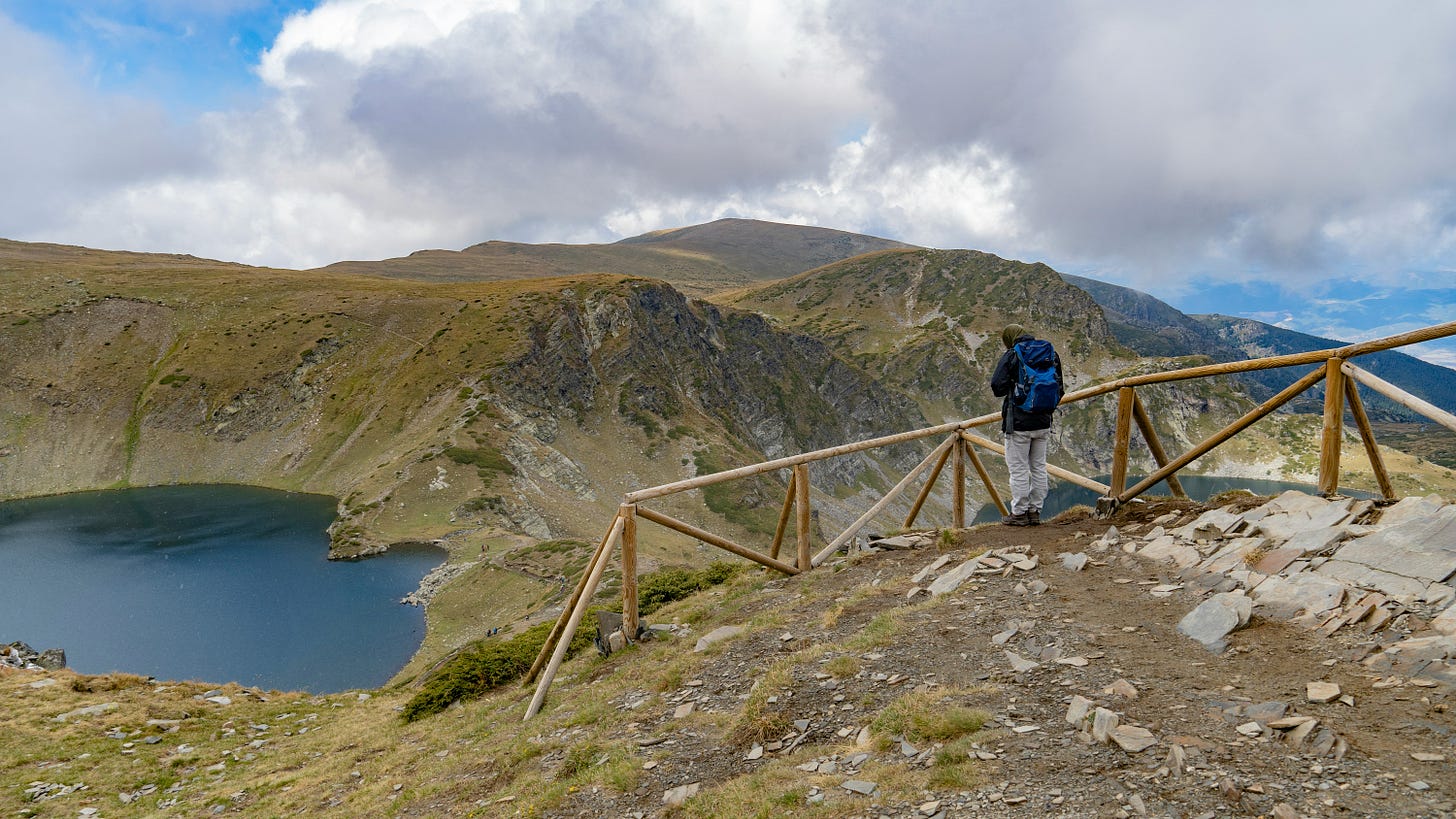 Image of man at a fence in the mountains overlooking a lake.