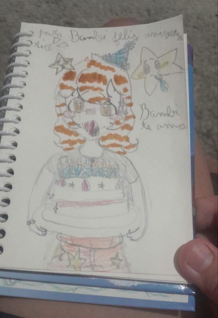 foto da página de um caderno com o desenho de uma menina feliz, segurando um bolo de aniversário, acompanhada por duas estrelinhas antropomórficas, uma delas está usando uma gravata. acima do desenho está escrito "para Bambi feliz aniversário", e do lado, "Bambi te amo". eu sou bambi e a meninha do desenho, que mesmo desenhada no estilo de uma criança de 10 anos, se parece muito comigo.